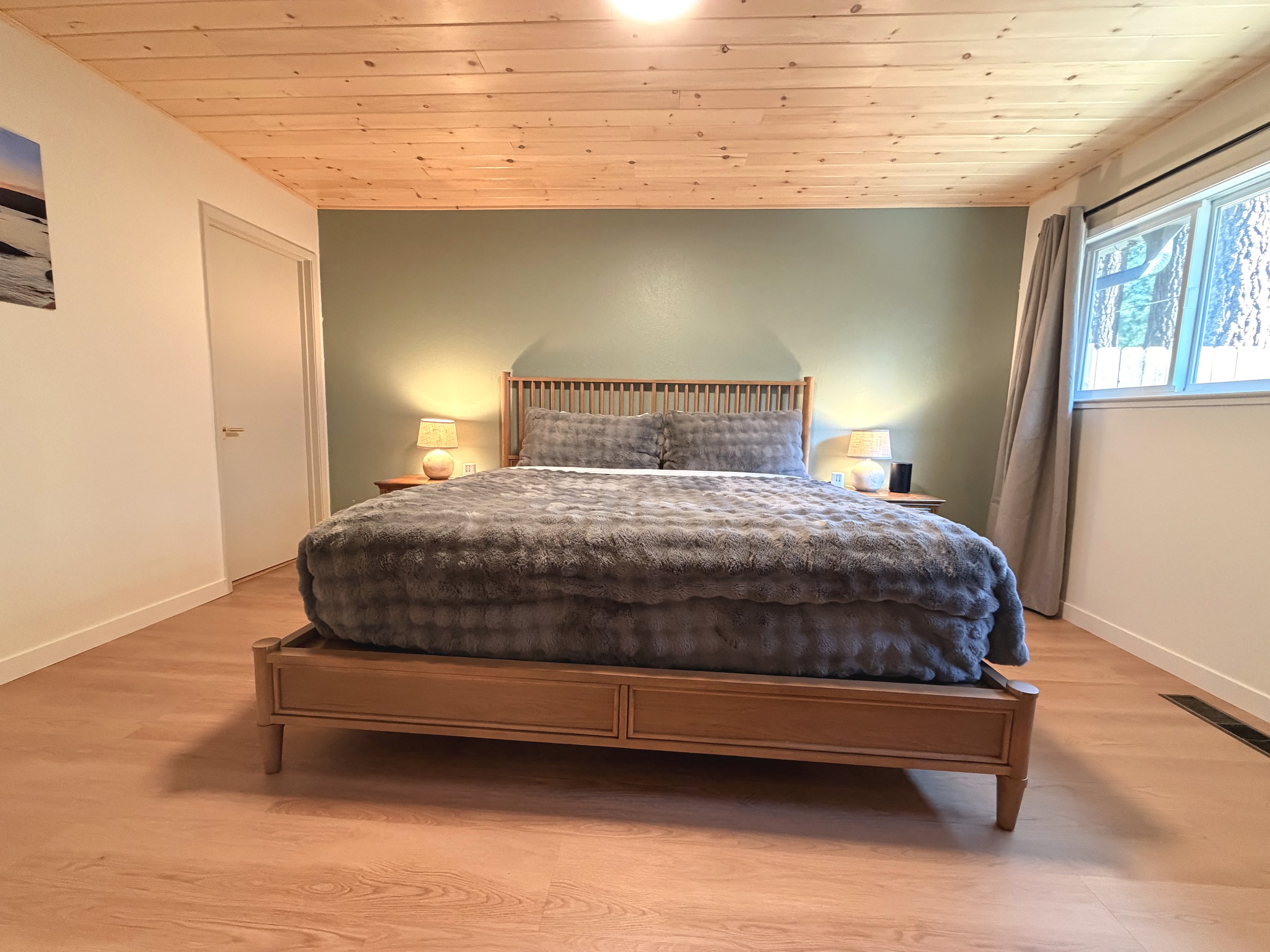 Primary bedroom — king bed against a sage accent wall under a pine ceiling