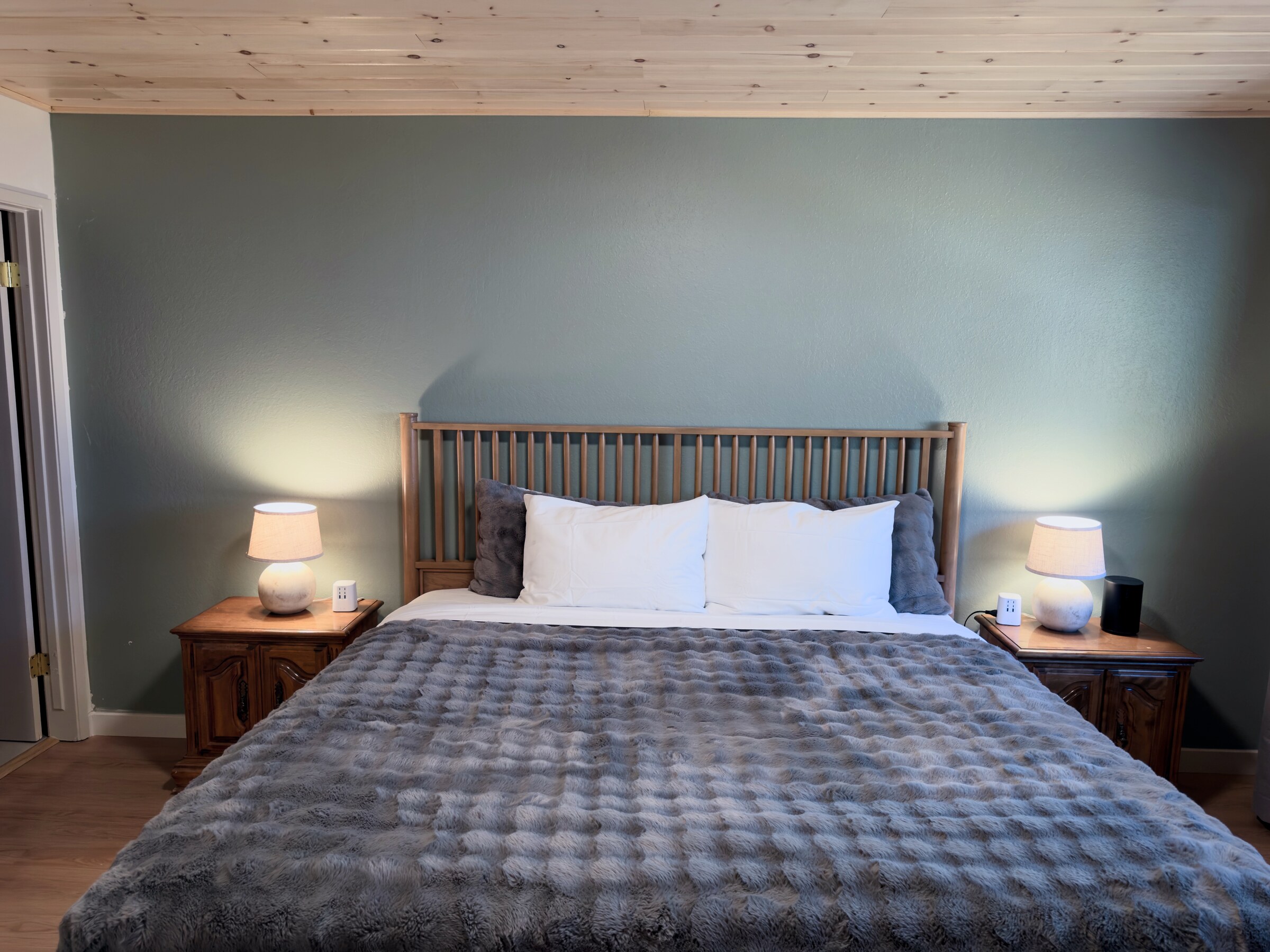 Primary bedroom — king bed against a sage accent wall under a pine ceiling